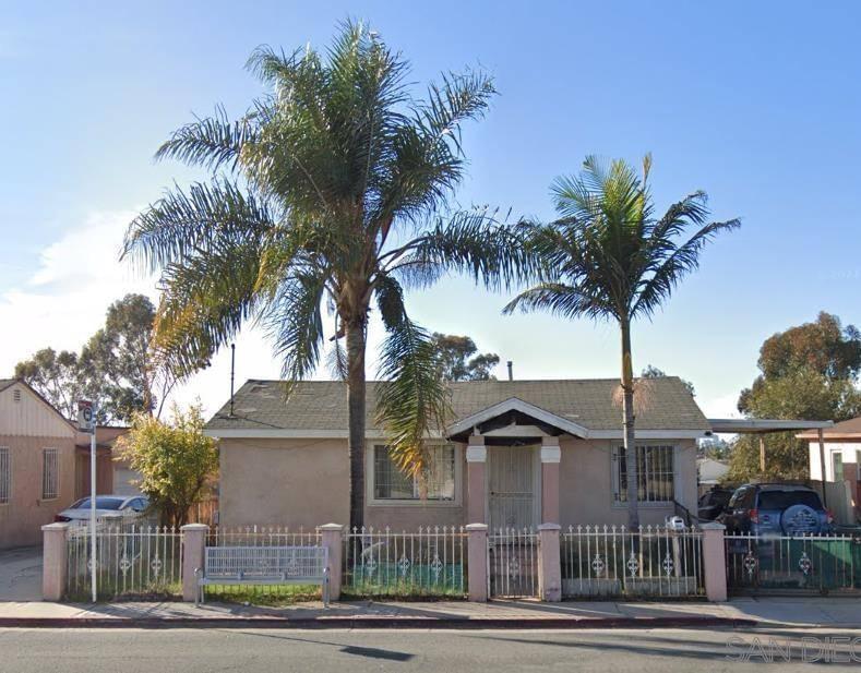 A beige stucco home with large palm trees and decorative fence